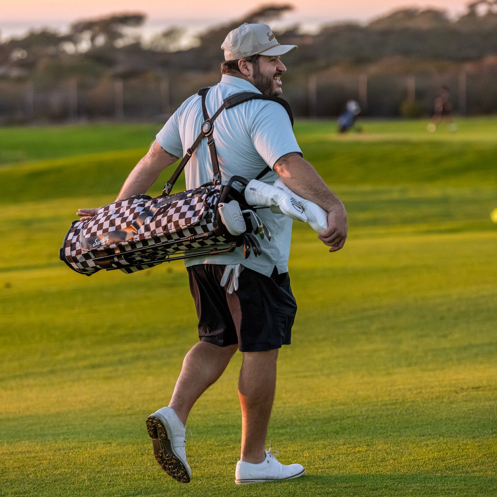 Man walking on a golf course carrying the Black/White Checker El Camino golf bag and clubs.