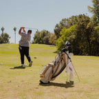 A man playing golf with his Ryder golf bag in toasted almond behind him