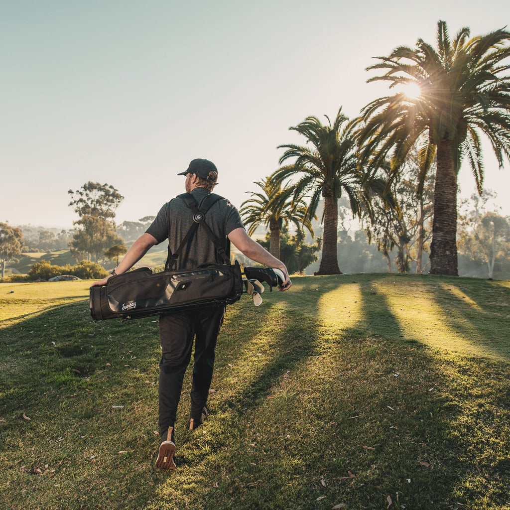 man carrying the matte black El Camino golf bag by Sunday golf on golf course with palm trees